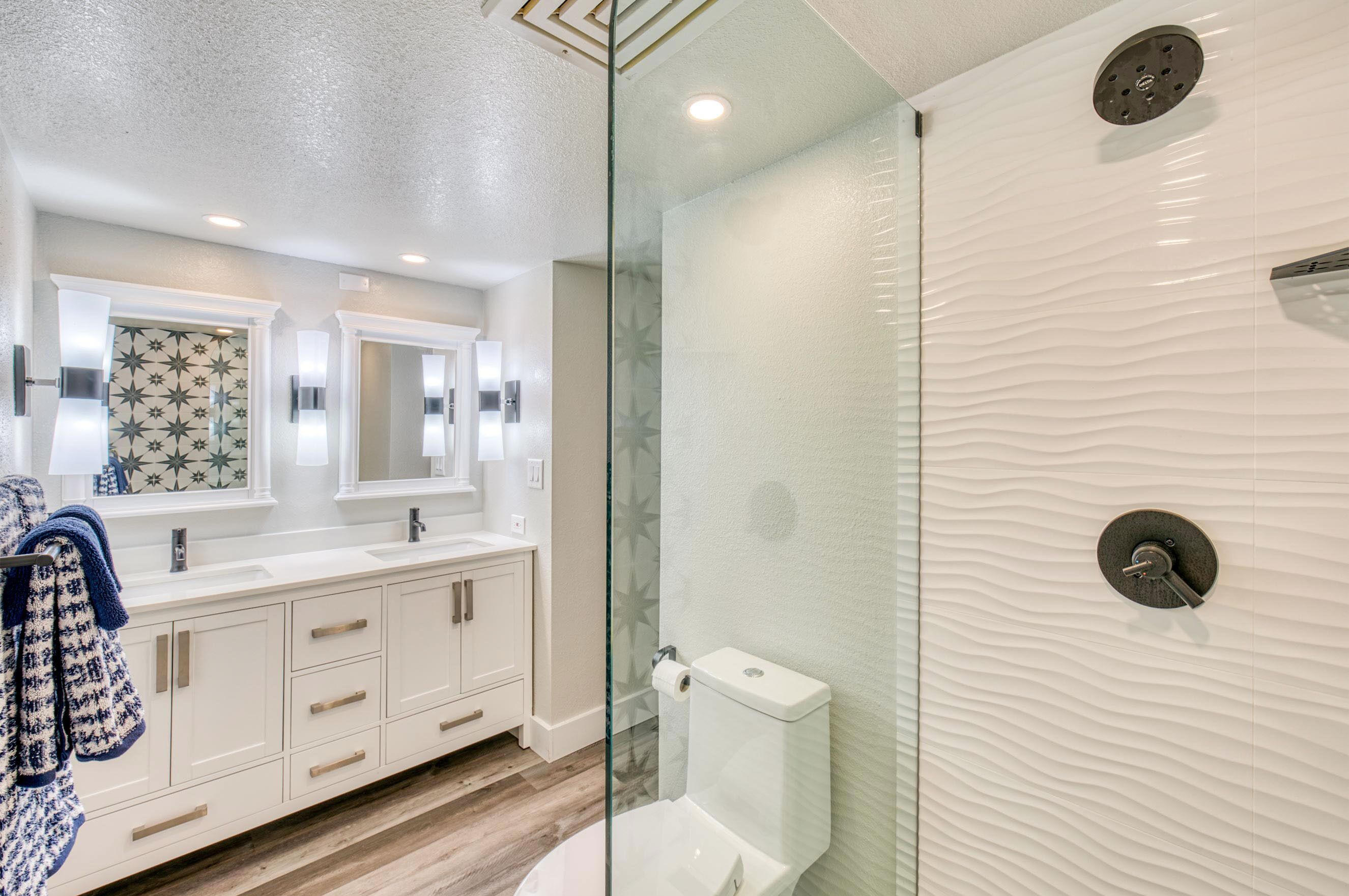 A modern bathroom with a glass-enclosed shower, a white vanity with a mirror, and a patterned backsplash.