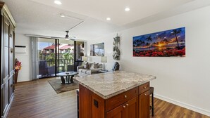 Amplia sala de estar con piso de madera, una isla en la cocina y un gran ventanal con vistas a un balcón.