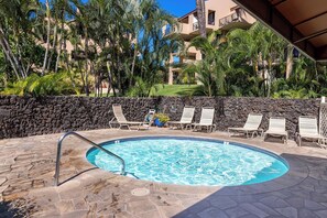A swimming pool with lounge chairs, a stone wall, and a building with balconies in the background. - Kamaole Sands 7-308 - Fully Renovated in 2025, Whisper-quiet AC, Premium Comfort (Kihei)