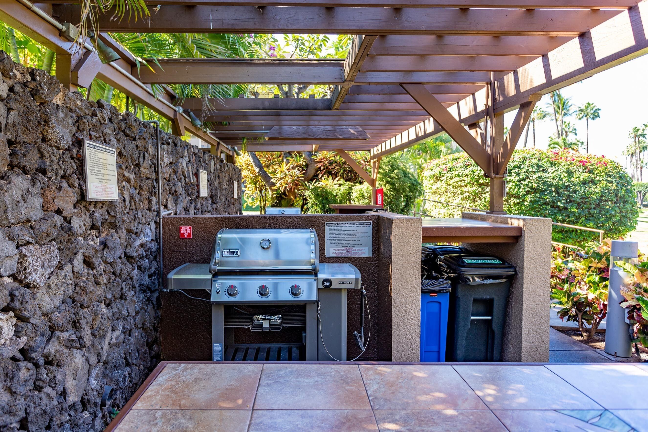 An outdoor barbecue area with a stone wall, a grill, and a trash bin.