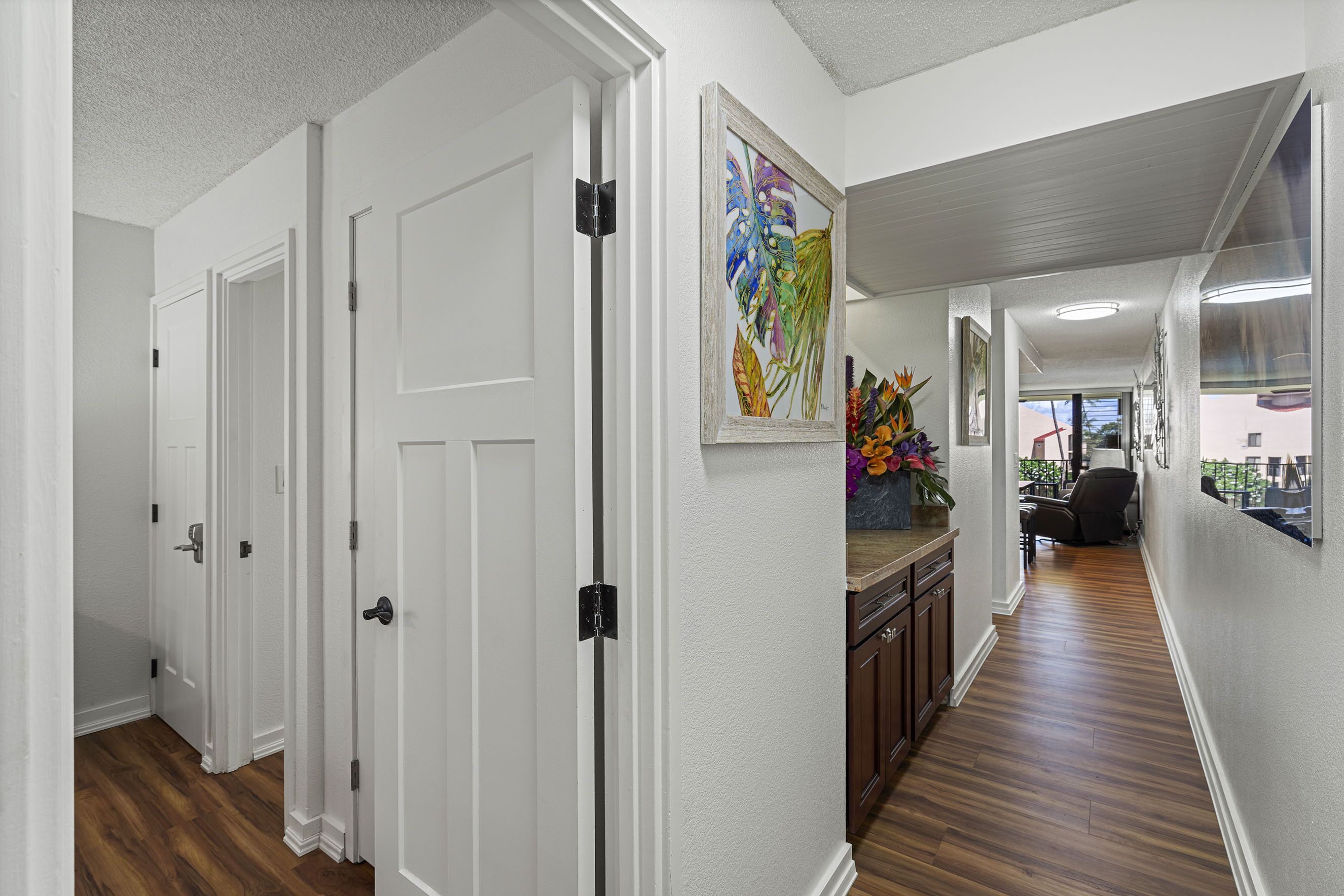 A hallway with white doors, wooden flooring, and a painting on the wall.