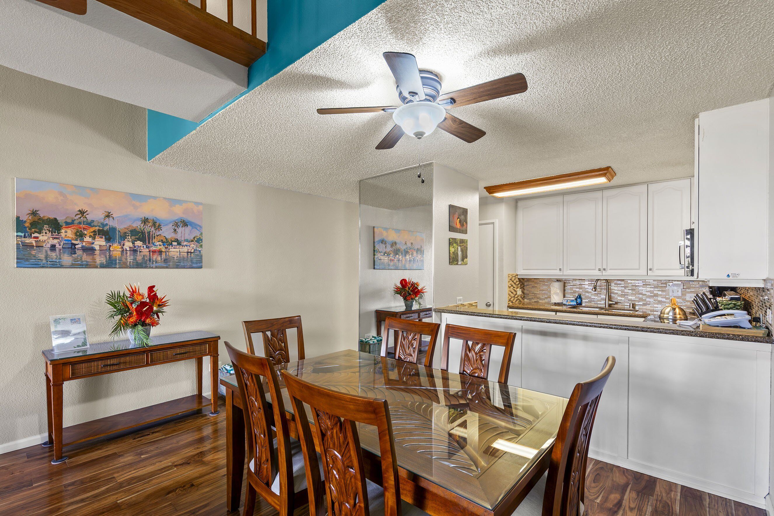 A dining area with a glass-top table, wooden chairs, and a ceiling fan.