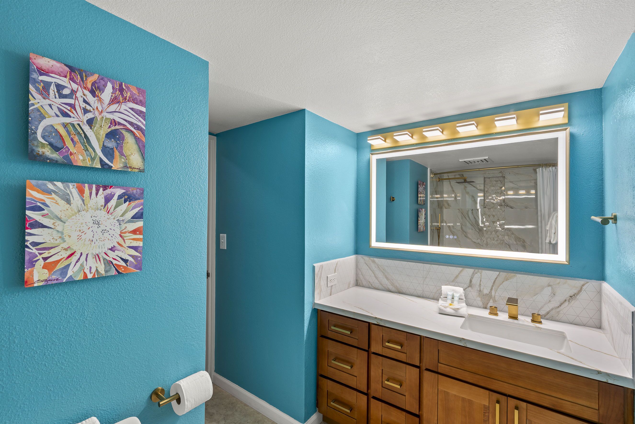 A bathroom with teal walls, a white sink, and wooden cabinets. There are two floral paintings on the wall.