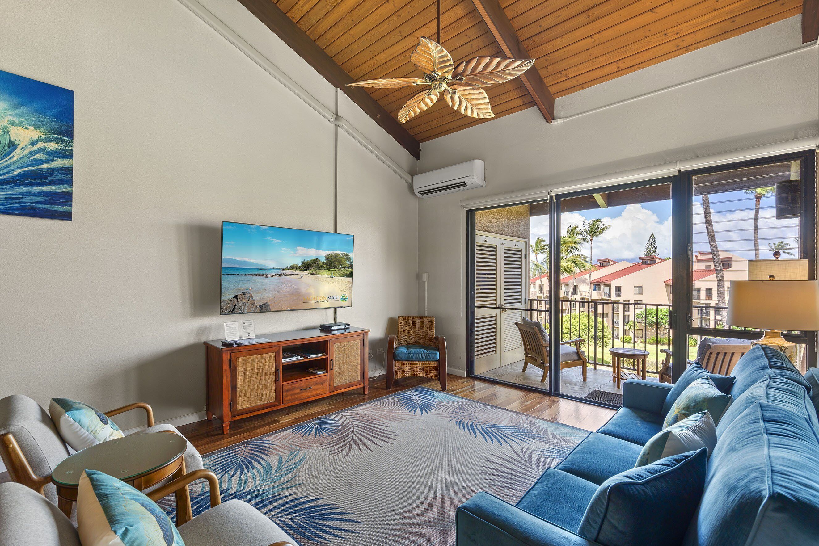 Un salon avec un canapé bleu, un téléviseur, un ventilateur de plafond et une vue sur le balcon extérieur.