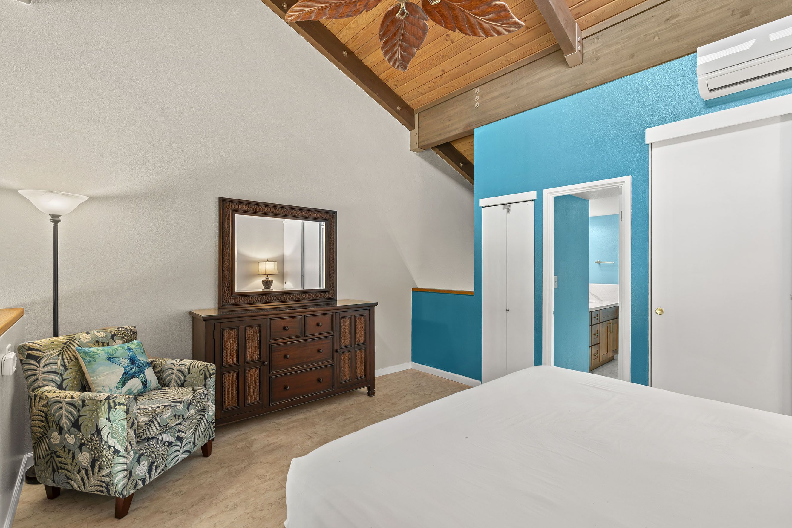 A bedroom with a bed, a dresser, a chair, and a mirror.