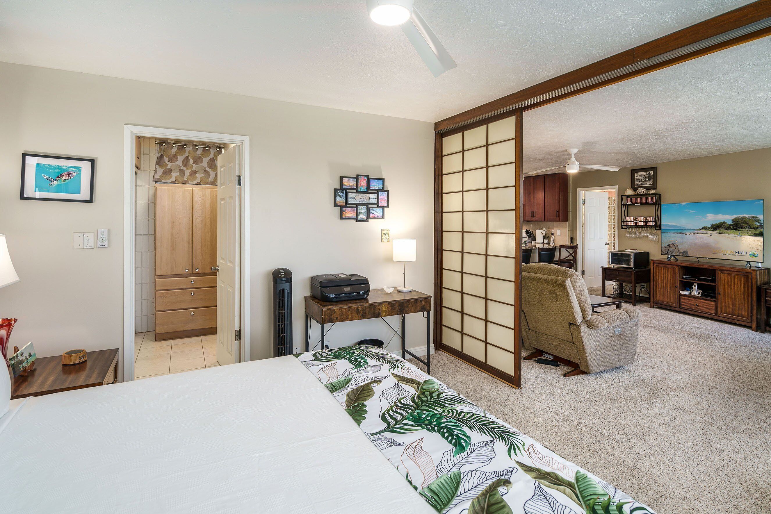 A hotel room with a bed, a desk, a chair, a TV, and a sliding door leading to another room.