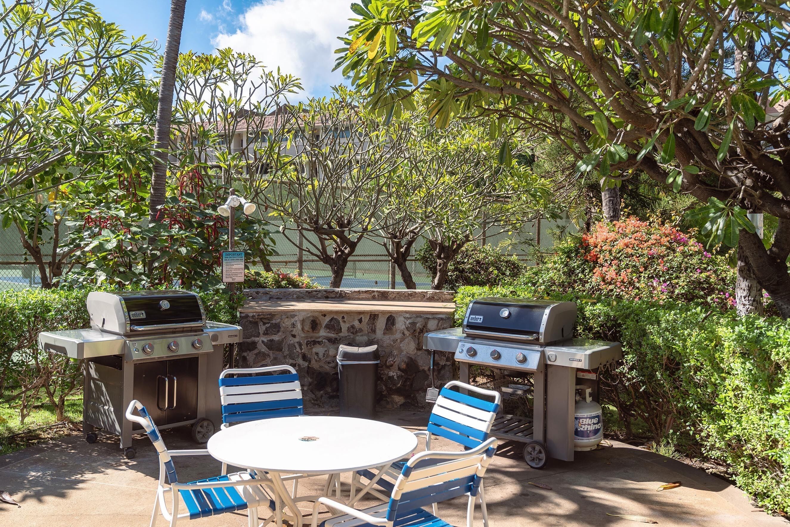 An outdoor patio with two barbecue grills, a round table, and blue-striped chairs.
