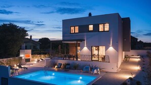 Une maison moderne à deux étages, dotée d’une piscine, d’un espace extérieur aménagé et d’un patio bien éclairé.