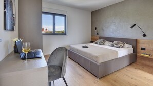 Une chambre avec un lit, un bureau avec un ordinateur portable et un verre de vin, une chaise et une fenêtre donnant sur un beau paysage.