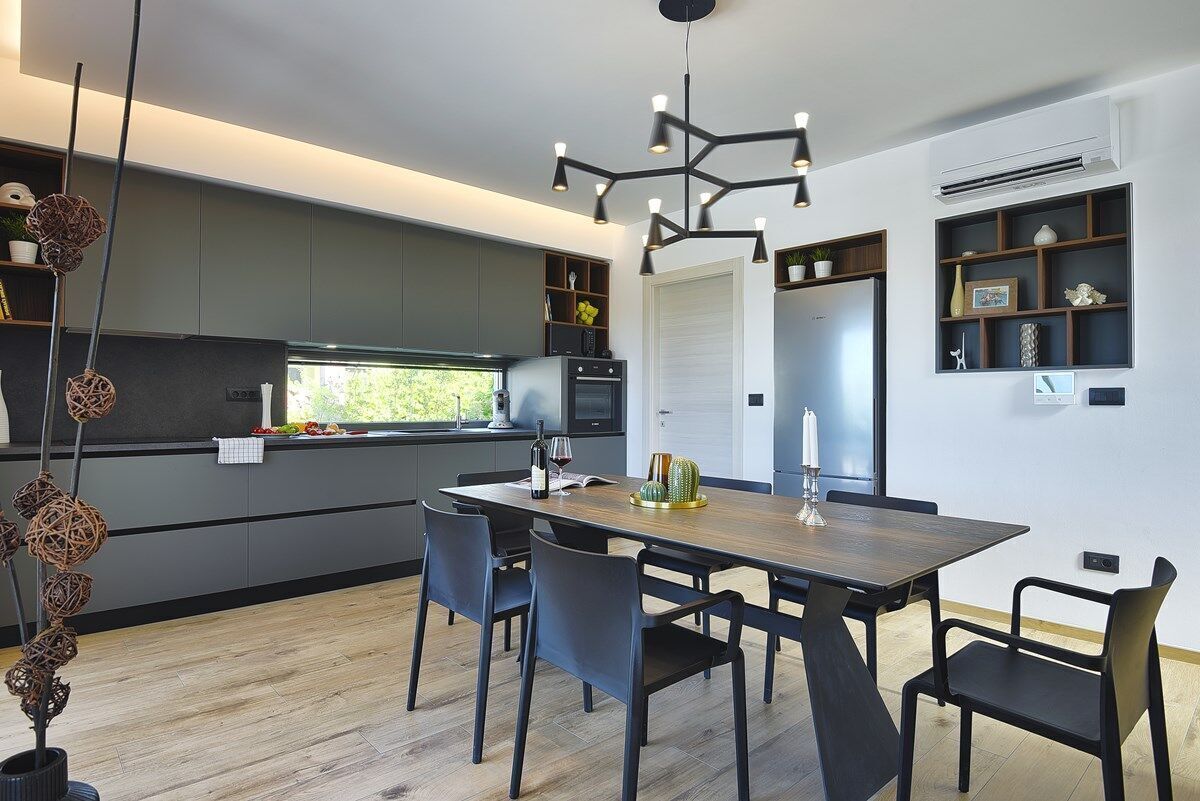 A modern kitchen with dark cabinets, a wooden dining table, and a unique pendant light.