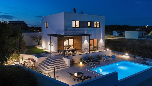 Une maison moderne à deux étages, dotée d’une piscine, d’un espace extérieur aménagé et d’un patio bien éclairé.