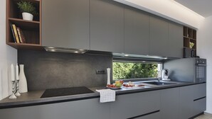 Une cuisine moderne avec des meubles de couleur grise, un plan de travail noir et une fenêtre donnant sur un paysage verdoyant.