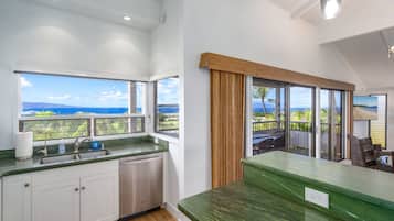 A modern kitchen with a view of the ocean, a large window, and a green countertop.