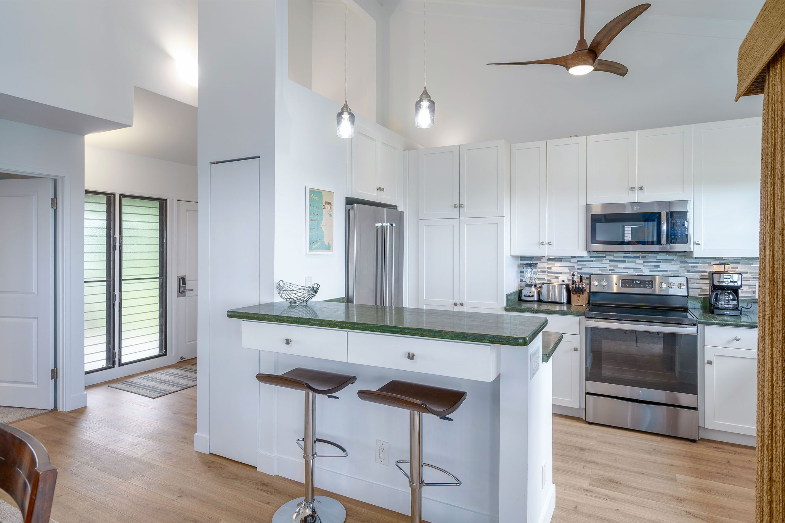 A modern kitchen with white cabinets, stainless steel appliances, and a green countertop island with two stools.