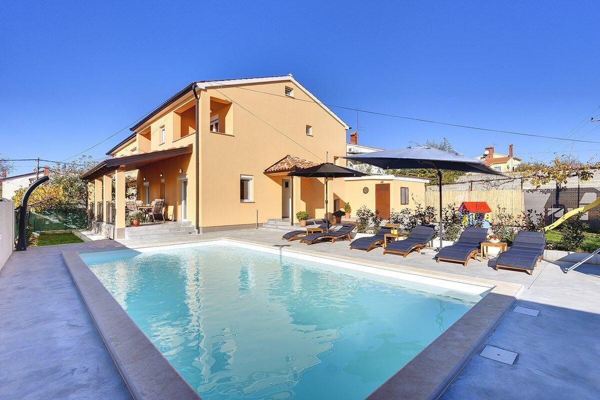 A two-story building with a swimming pool, lounge chairs, and a covered patio area.