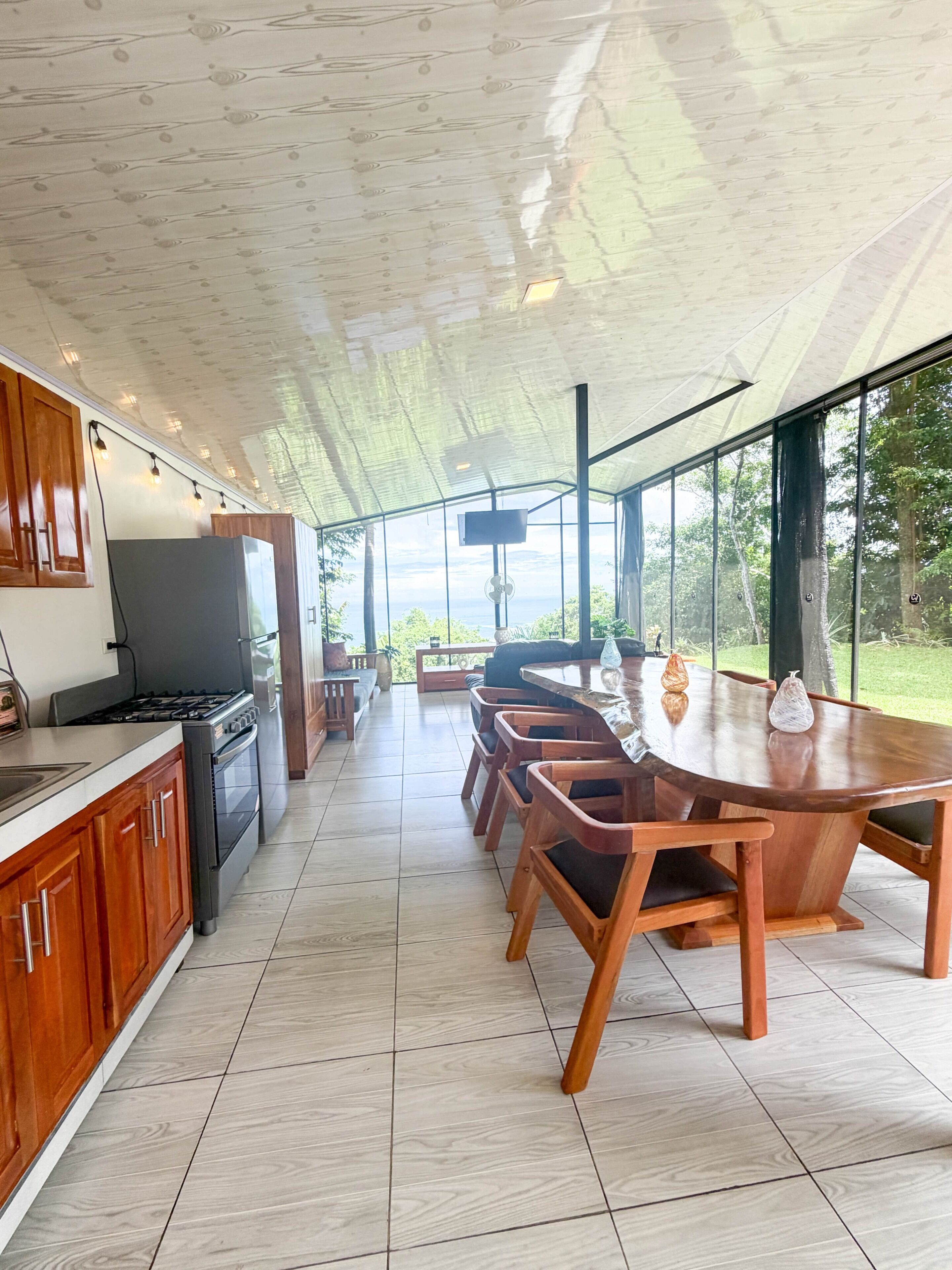 A modern kitchen with a dining area, large windows, and a TV.