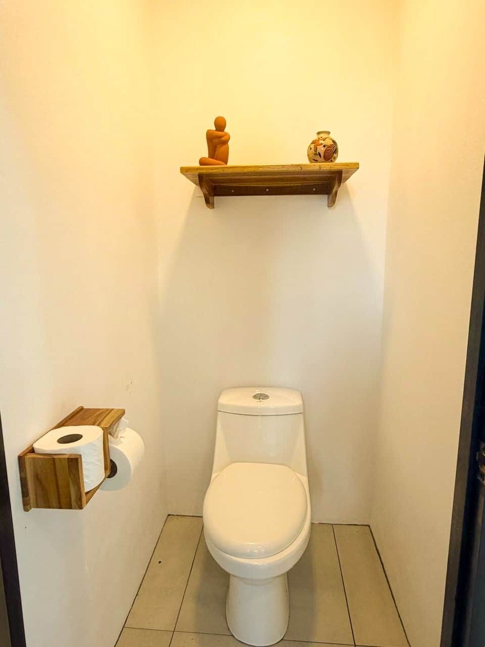 A small bathroom with a toilet, a shelf with a vase, and a roll of toilet paper.