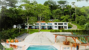 Une maison moderne dotée d’une piscine, d’un espace salon extérieur et d’un escalier menant à l’entrée.