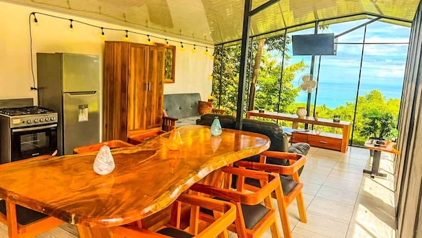 Un vaste espace dédié à la salle à manger, avec une longue table et des chaises en bois, une cuisine équipée d’appareils modernes et une grande baie vitrée donnant sur l’extérieur.