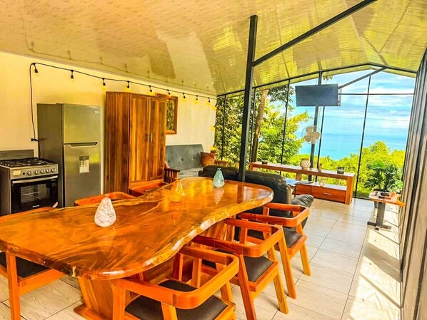 Un vaste espace dédié à la salle à manger, avec une longue table et des chaises en bois, une cuisine équipée d’appareils modernes et une grande baie vitrée donnant sur l’extérieur.