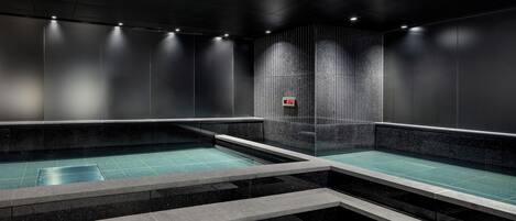 Una piscina interior moderna con agua cristalina, rodeada de paredes oscuras y escalones que bajan a la piscina.
