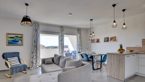 Un saló modern amb un sofà gris, un armari blau i una zona de menjador amb taula i cadires.