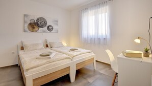 Un dormitori modern amb un llit doble, un escriptori i una cadira. Hi ha un quadre a la paret i una finestra amb cortines.