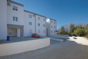 A modern building with multiple floors, a red car parked in front, and a gravel driveway. - Apartment Barbara (74235-A1) - Medulin (Medulin)