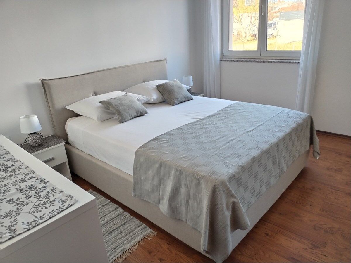 Une chambre à coucher avec un lit, une table de chevet, une lampe et une vue sur l’extérieur par une fenêtre.