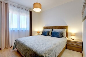 Ein ordentlich eingerichtetes Schlafzimmer mit einem Bett, Nachttischlampen und einem Fenster mit Vorhängen.