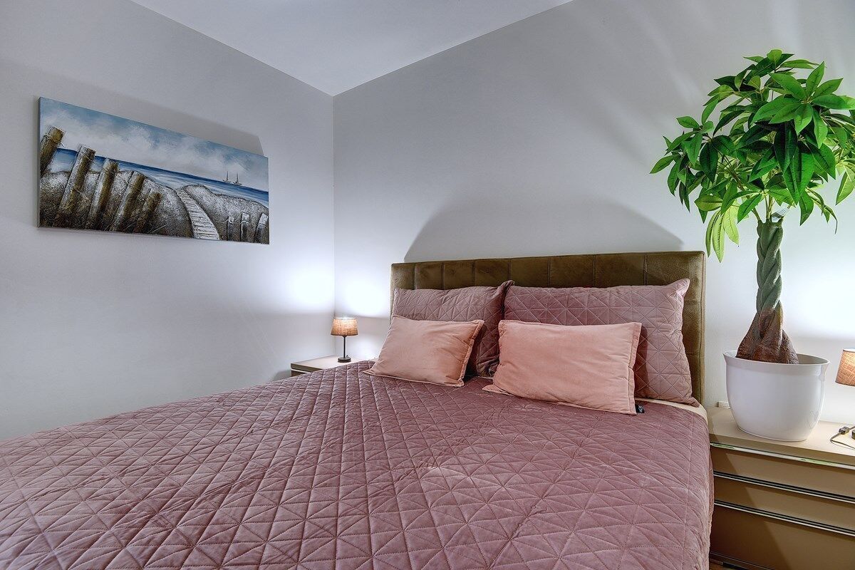 Ein Schlafzimmer mit einem großen Bett, einem Kopfteil, einem Nachttisch, einer Lampe und einer Zimmerpflanze.