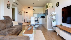 A modern living room with a sofa, coffee table, and TV stand. There is a kitchen in the background with cabinets and a dining area. - Apartment Beach (74259-A1) - Medulin (Medulin)