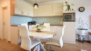 A modern kitchen with white cabinets, a dining table with chairs, a hanging light fixture, a microwave, and a clock on the wall. - Apartment Beach (74259-A1) - Medulin (Medulin)