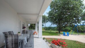 Un patio al aire libre con una mesa y sillas de comedor, un conjunto de columpios y un gran árbol de fondo.