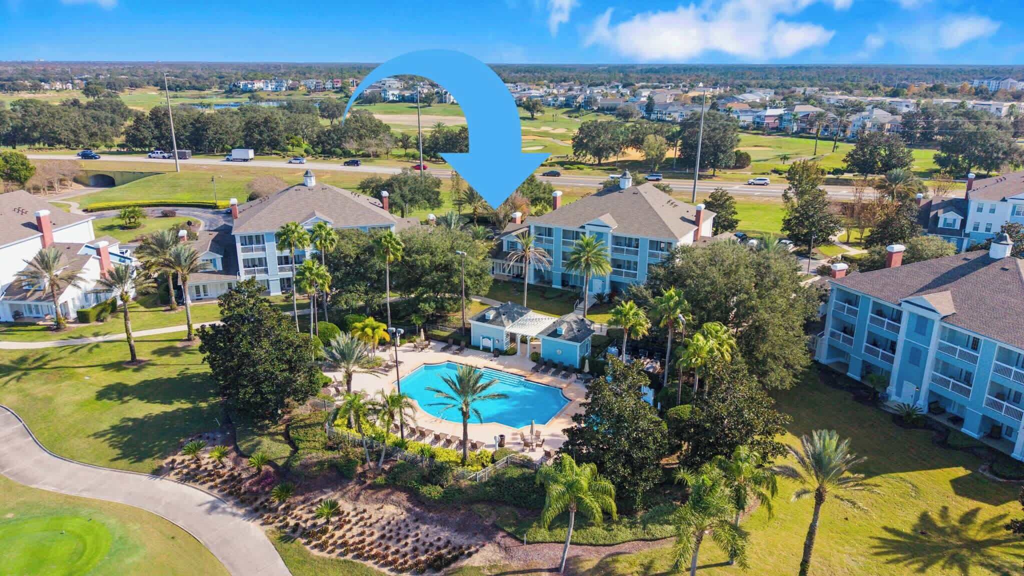 A resort with multiple buildings, a central swimming pool, and surrounding greenery.
