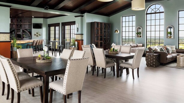 A spacious dining area with a dark wooden table and upholstered chairs, large windows offering a view, and a high ceiling with exposed beams. - Sandy Ridge Retreat Just Steps from the Splash Pad (Kissimmee)