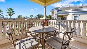 A covered outdoor seating area with a round table and chairs, a potted plant, and a view of a building with a balcony. - Sandy Ridge Retreat Just Steps from the Splash Pad (Kissimmee)