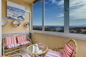 Un balcon agrémenté de meubles en osier, d’un tableau et offrant une vue sur la mer et le paysage.