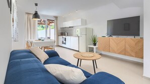 Een moderne woonkamer met een blauwe bank, een klein rond tafeltje en een televisie op een houten kast.