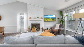 Una sala moderna con un sofá gris, una chimenea, un televisor y un ventanal grande.
