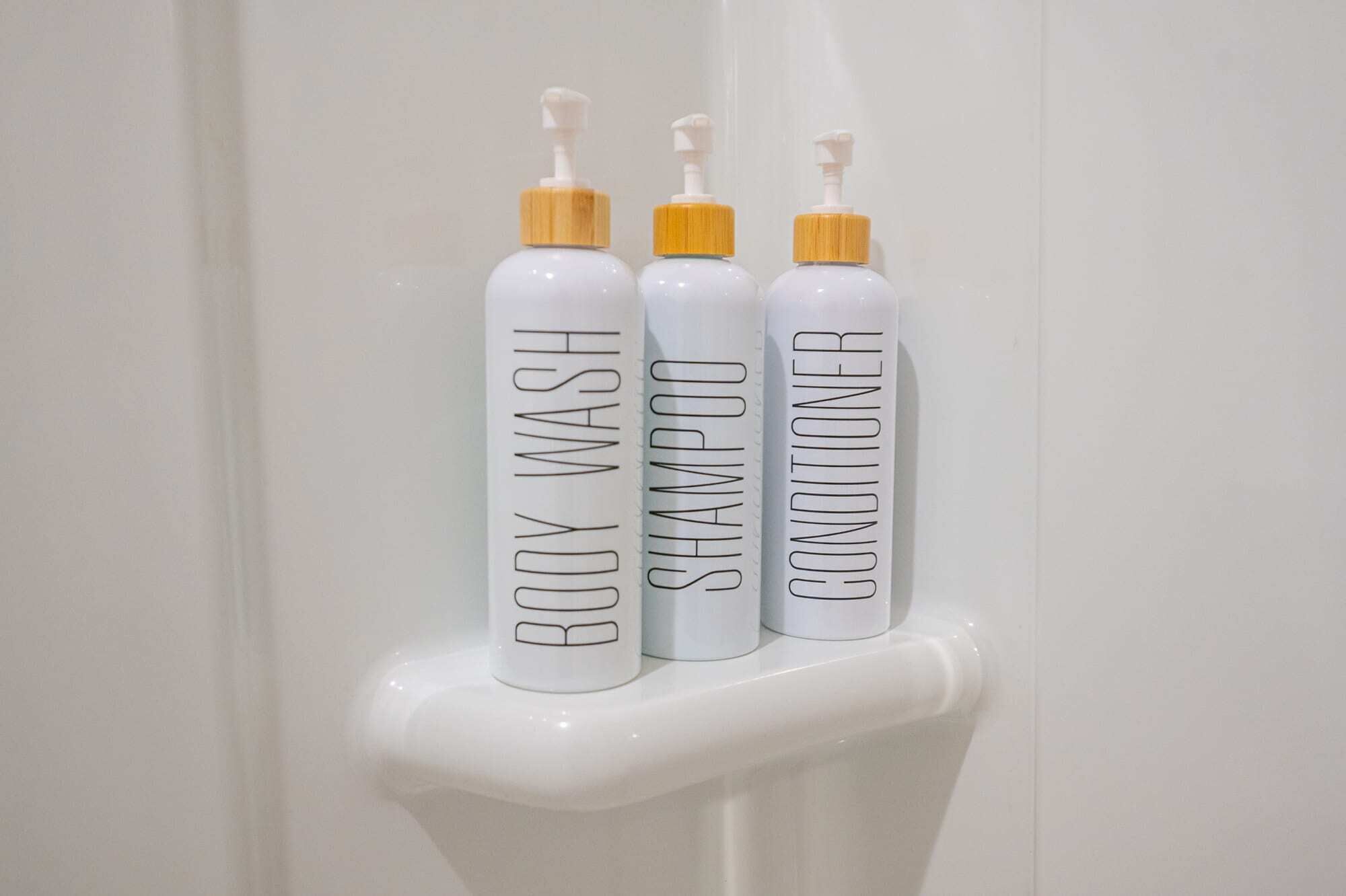 Tres botellas de gel de baño, champú y acondicionador sobre una superficie blanca.