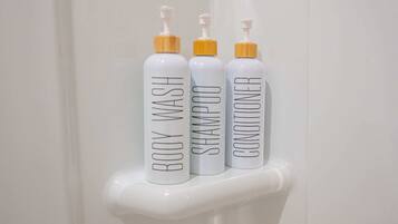 Tres botellas de gel de baño, champú y acondicionador sobre una superficie blanca.