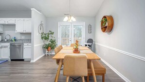 Una cocina moderna con armarios blancos, lavavajillas de acero inoxidable y un comedor con mesa y sillas de madera.