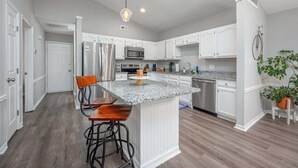 Una cocina moderna con armarios blancos, encimera de granito, electrodomésticos de acero inoxidable y una barra con taburetes.
