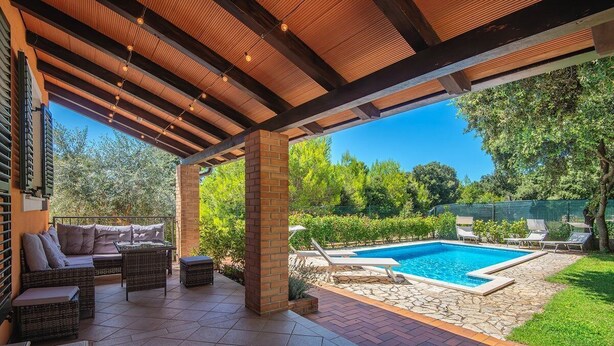 Un patio al aire libre con piscina, zona de estar y una pérgola con guirnaldas de luces.