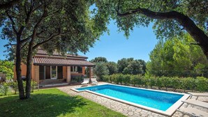 Una piscina rectangular con borde de piedra, rodeada por un césped cuidado y árboles.