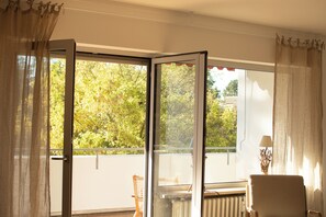 A room with a large sliding glass door leading to a balcony, a chair, and a table.
