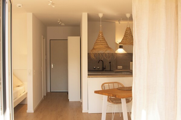 A modern kitchen with a wooden table and chairs, a hanging woven light fixture, and a white door in the background.