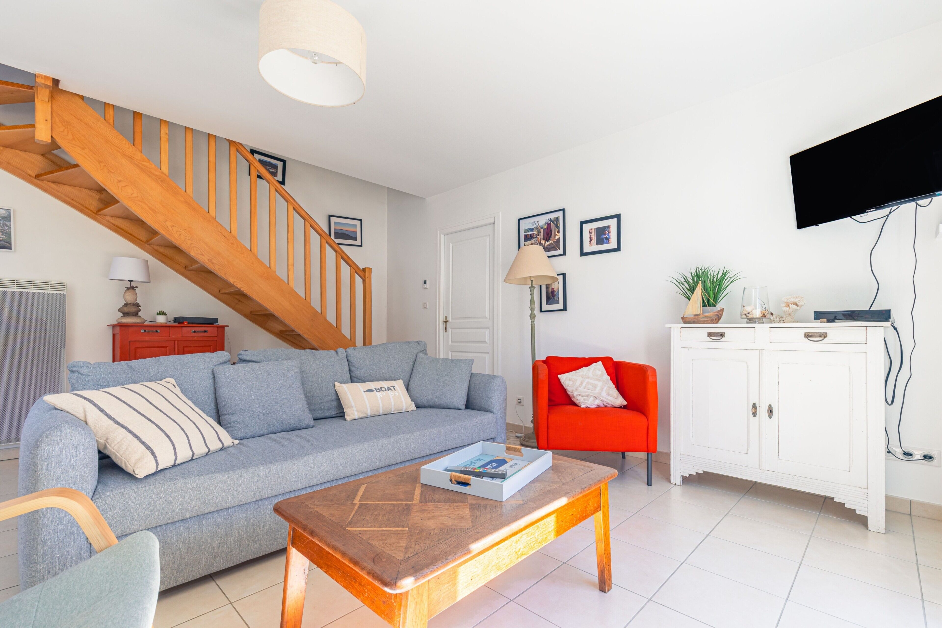 Ein Wohnzimmer mit einer Couch, einem Couchtisch, einem roten Sessel, einem weißen Schrank und einer Holztreppe.