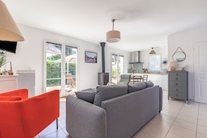 A modern living room with a grey sofa, a red chair, and a kitchen in the background. - Charming Seaside Retreat with Private Garden and Terrace (Saint-Georges d'Oléron)